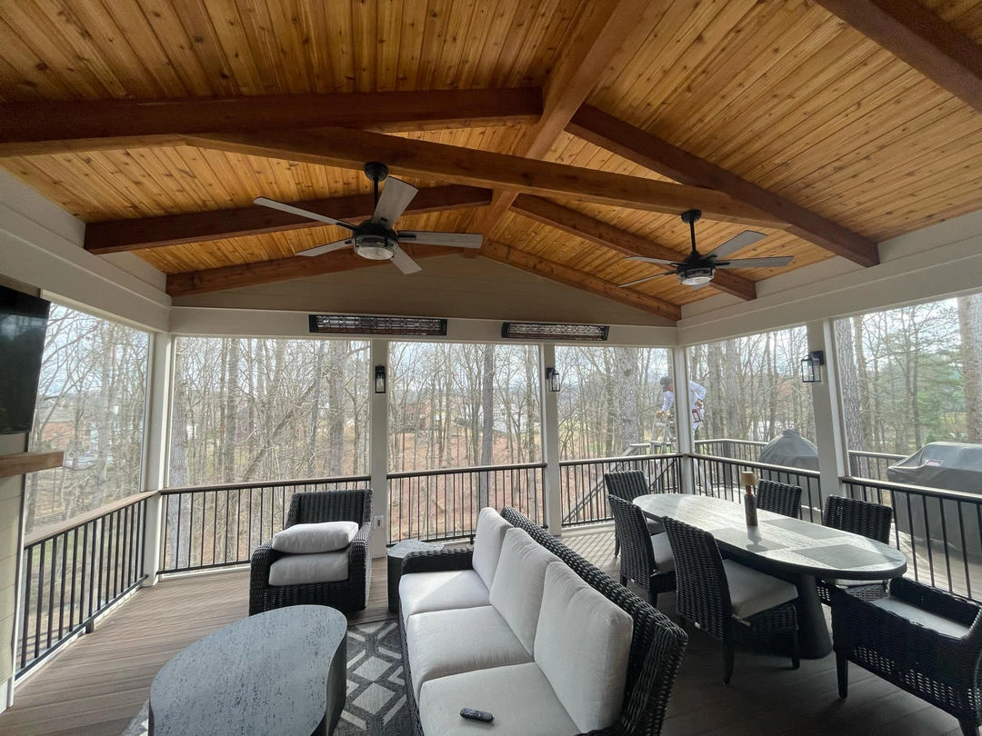 A screened-in porch with a wooden vaulted ceiling, two ceiling fans, and modern outdoor furniture.